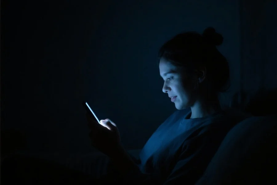 用户在昏暗环境下使用APP，屏幕显示为深色夜间模式，人物表情专注且舒适